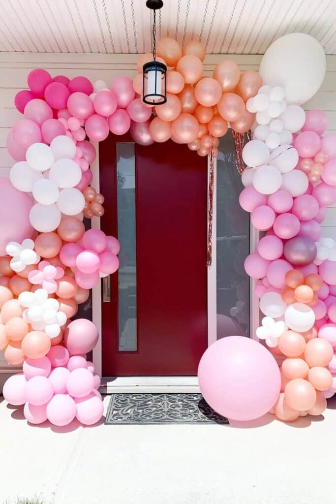 pink, white and peach balloon arch over a red door