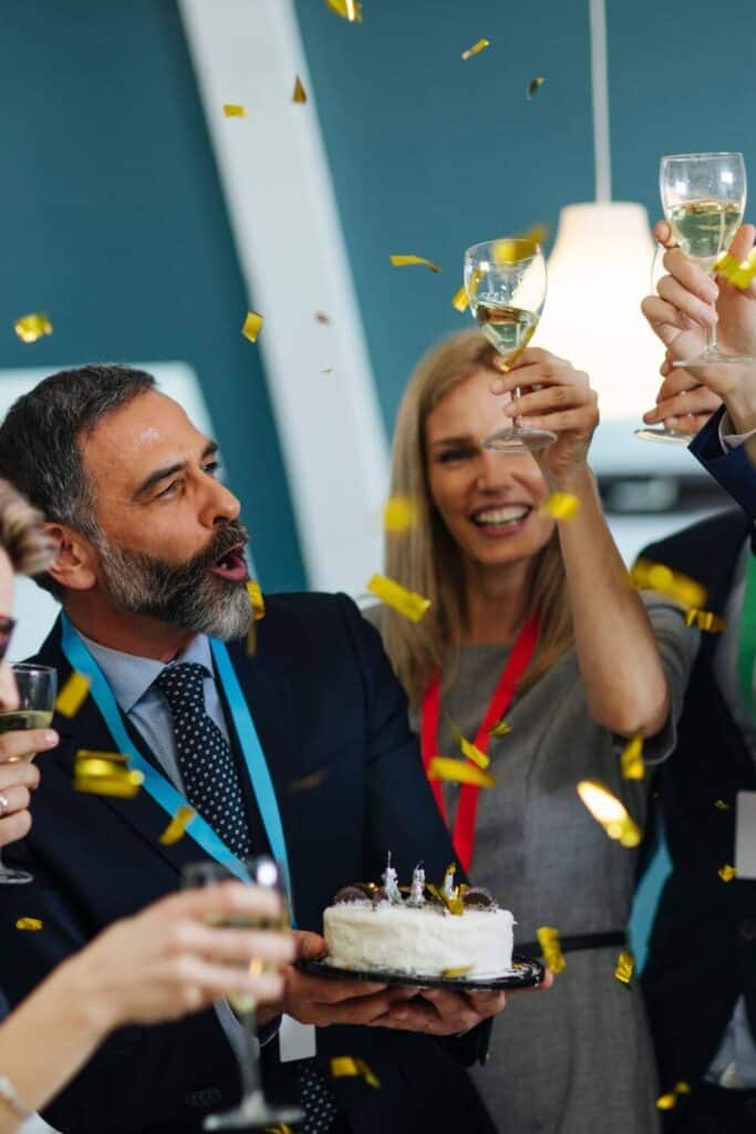 coworkers lifting glasses of wine to toast a man with a small retirement cake in his hands